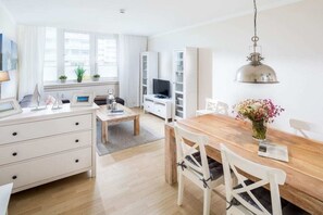 A modern living room with a dining area, white furniture, and a large window providing natural light. - Kaiserhof 002 Reinke am Strand (Norderney)