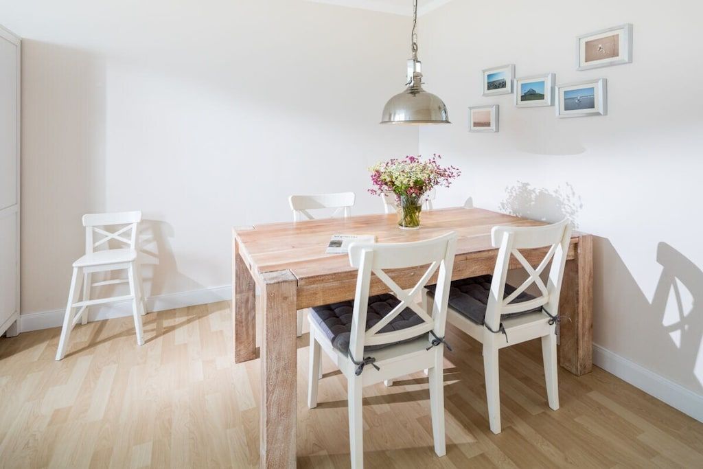 A dining area with a wooden table, white chairs, and a hanging light fixture.
