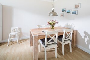 A dining area with a wooden table, white chairs, and a hanging light fixture. - Kaiserhof 002 Reinke am Strand (Norderney)