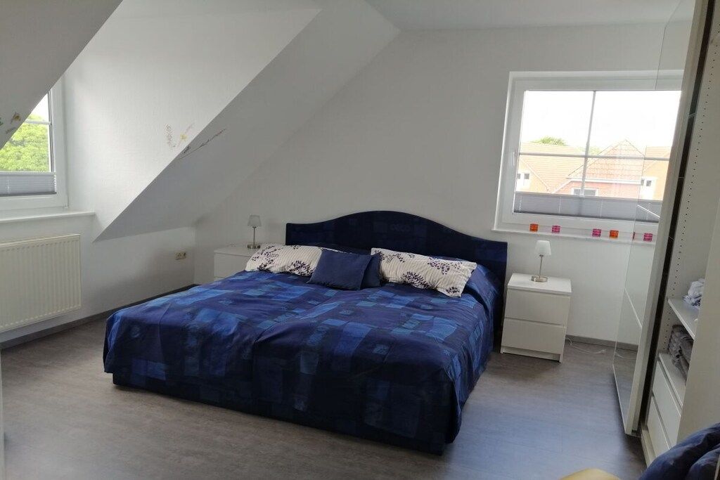 A bedroom with a bed, a nightstand, a window, and a radiator.
