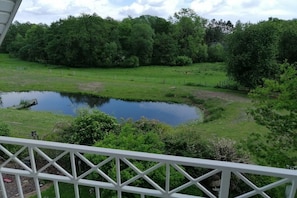 A pond surrounded by lush greenery, a white fence, and a white railing. - Holiday apartment in Süsel with swimming pool (Süsel)