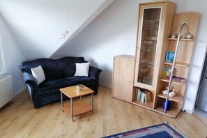 A room with a dark blue patterned sofa, a wooden cabinet with glass doors, and a small wooden table. - Holiday apartment in Süsel with swimming pool (Süsel)