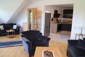 A living room with a sofa, a coffee table, and a kitchen area with a refrigerator and cabinets. - Holiday apartment in Süsel with swimming pool (Süsel)