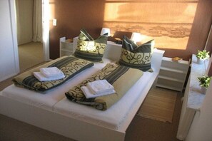 Une chambre d’hôtel avec un lit, des oreillers, une table de chevet, une lampe et une petite plante.