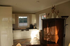 A kitchen with a window, cabinets, a coffee maker, and a cabinet with decorative items. - Jona with sauna/fireplace (Schönberg)