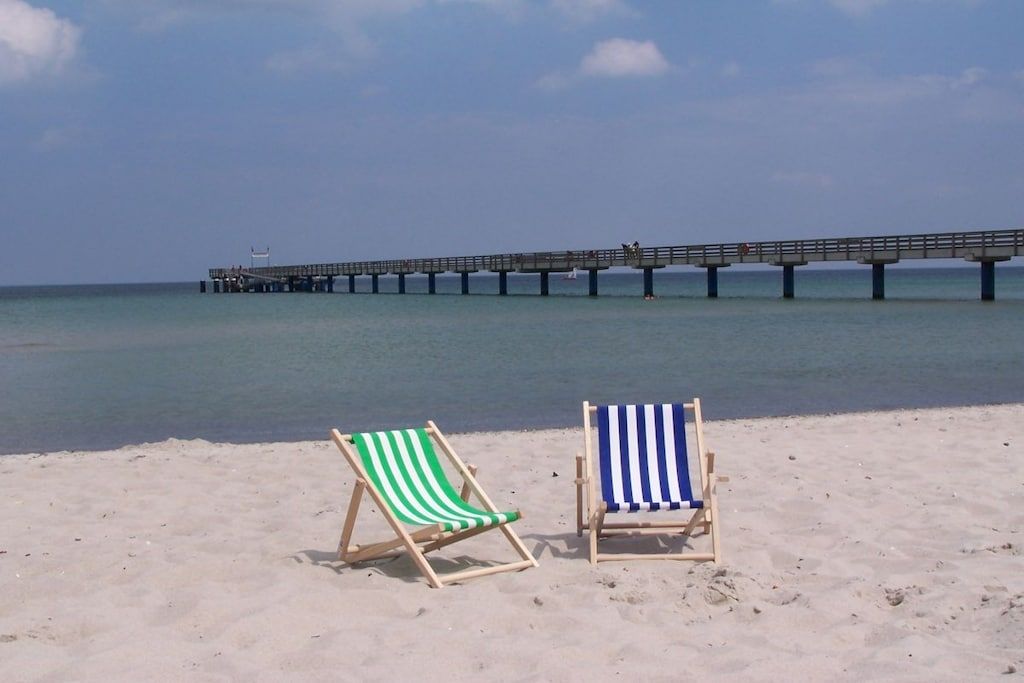Deux chaises de plage sur une plage de sable, avec une jetée en arrière-plan.