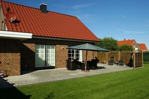A brick house with a red tiled roof, a patio with outdoor furniture, and a satellite dish. - Jona with sauna/fireplace (Schönberg)