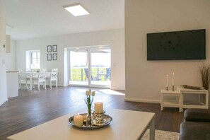 Un salon moderne comprenant un coin repas, un téléviseur à écran plat fixé au mur et un balcon avec vue.