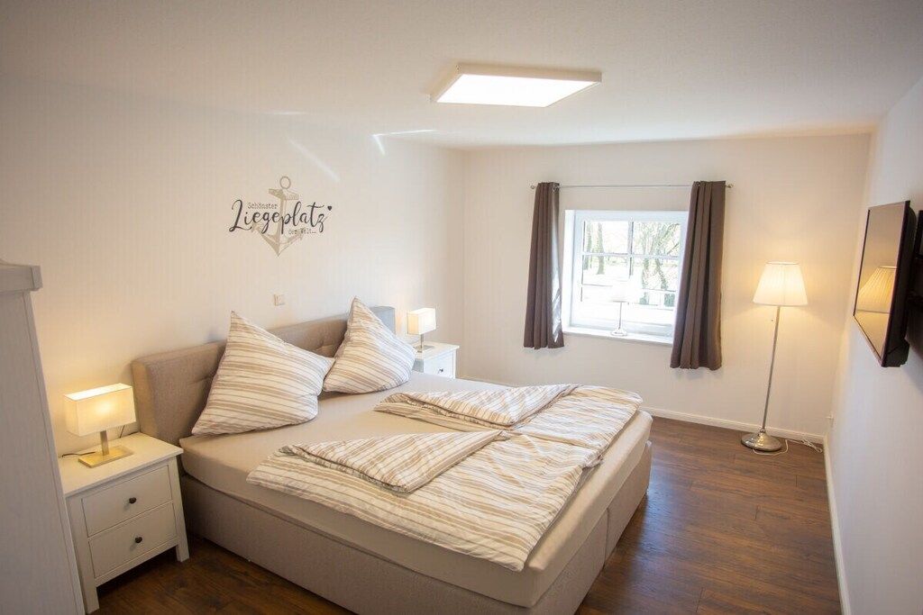 Une chambre à coucher comprenant un lit, des lampes de chevet, une table de nuit, une fenêtre avec des rideaux et un élément décoratif mural.