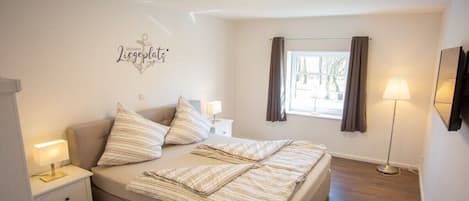 Un dormitorio con cama, lámparas de noche, mesita de noche, una ventana con cortinas y un adorno en la pared.