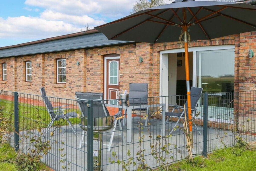 A brick building with a covered patio area, outdoor seating, and a fenced garden.