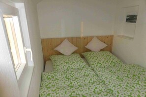 Un dormitorio con cabecera de madera, dos almohadas y una colcha verde estampada.