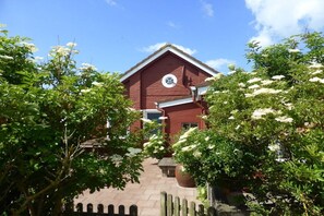 Ein rotbacksteiner Gebäude mit einer Uhr an der Fassade, umgeben von üppiger Bepflanzung und weißen blühenden Pflanzen.