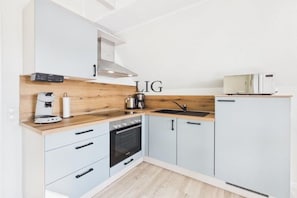 A modern kitchen with a wood accent wall, a coffee maker, a kettle, a microwave, and a stove. - Holiday apartment Sanddorn (Langeoog)