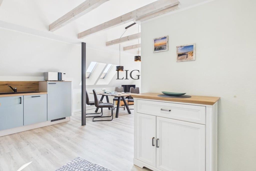A modern kitchen with light wood cabinets, a white countertop, and a dining area with a table and chairs.