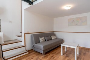 A room with a grey sofa, a white table, and a staircase with wooden steps. - A charming 43 sqm apartment, on the ground floor of a building (with about ten steps leading up from the main entrance) in a quiet residential area of ​​Catania, ideal for 3 guests. Functional and cozy, it is located in the Libertà-Stazione district (Catania)