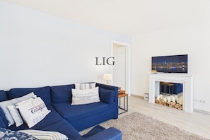 A living room with a blue sofa, a fireplace, and a television on the wall. - Holiday apartment Sandpiper (Langeoog)