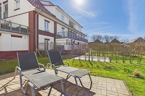 A two-story building with a balcony, outdoor seating area with chairs, and a well-maintained lawn. - Holiday apartment Sandpiper (Langeoog)