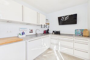 A modern kitchen with white cabinets, a stainless steel sink, and a black backsplash. - Holiday apartment Sandpiper (Langeoog)