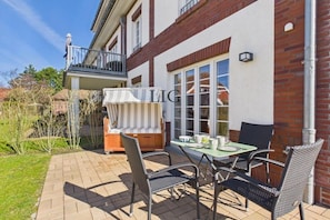 A patio with a table and chairs, a covered seating area, and a building with a balcony. - Holiday apartment Sandpiper (Langeoog)