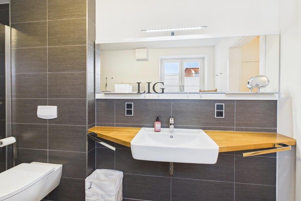 Une salle de bain avec un lavabo blanc, un plan de toilette en bois et un miroir au-dessus.