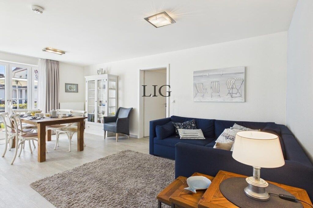 A modern living room with a blue sofa, a dining table with chairs, and a lamp on a side table.