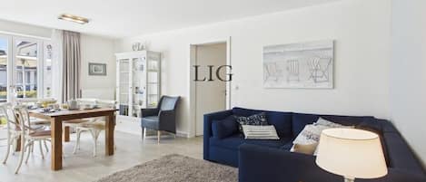Un salon moderne avec un canapé bleu, une table à manger avec des chaises et une lampe sur une table d’appoint.