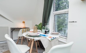 Uma área de refeições com mesa posta para dois, uma luminária e vista para o exterior pela janela.