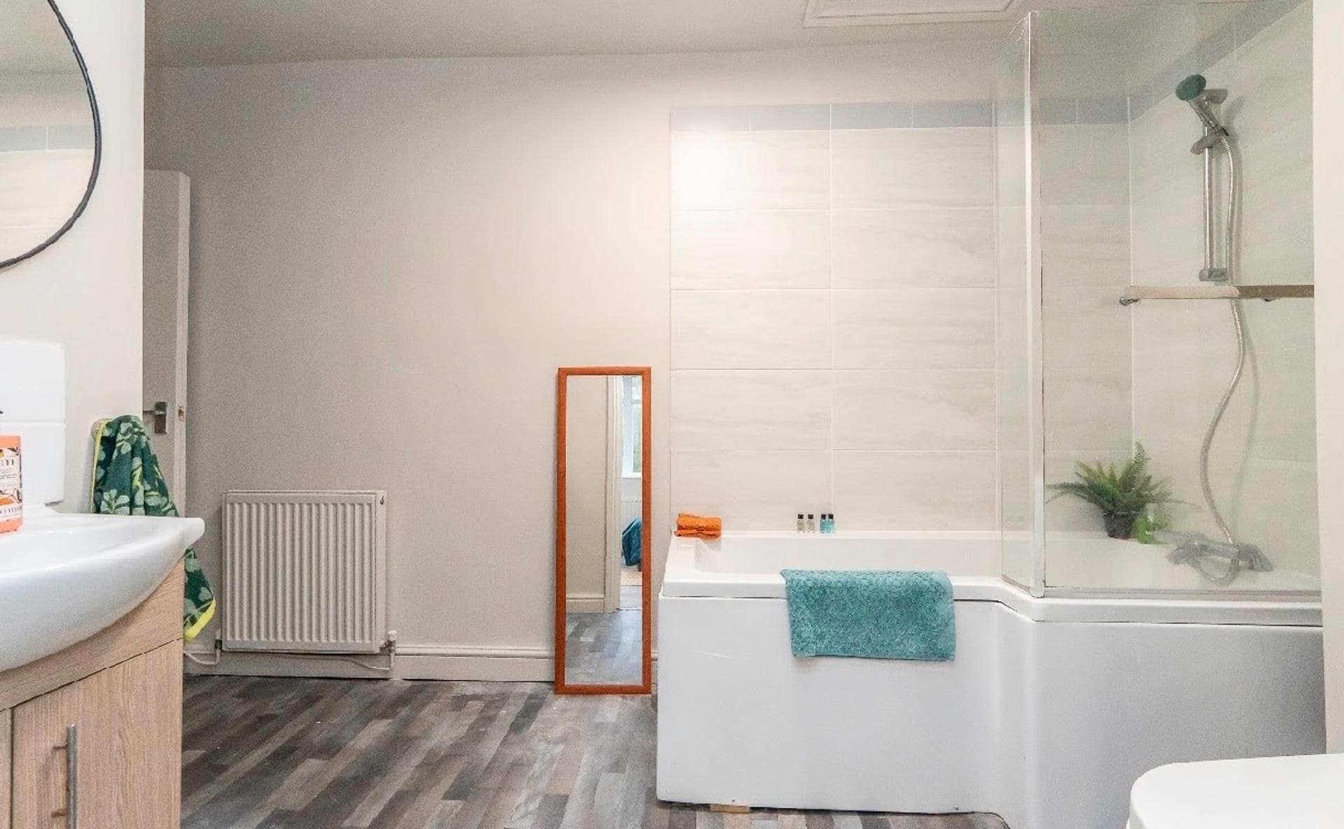 A bathroom with a white bathtub, a shower, a mirror, and a radiator.