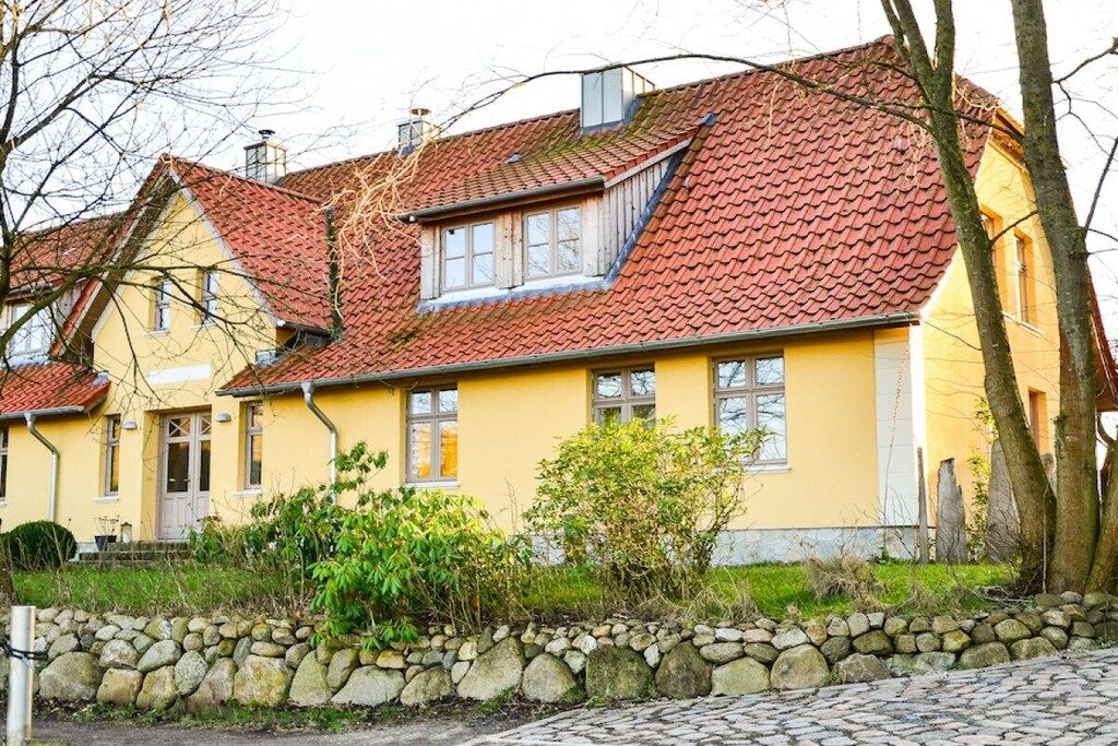 A yellow house with a red-tiled roof and a stone wall in front.