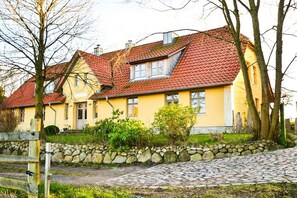 A yellow building with a red-tiled roof, a stone wall, and a cobblestone path. - Holiday apartment with 2 bedrooms (Wahlstorf-Wielen)