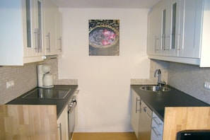 A compact kitchen with white cabinets, a coffee maker, a sink, and a decorative wall piece. - Holiday apartment with 2 bedrooms (Wahlstorf-Wielen)