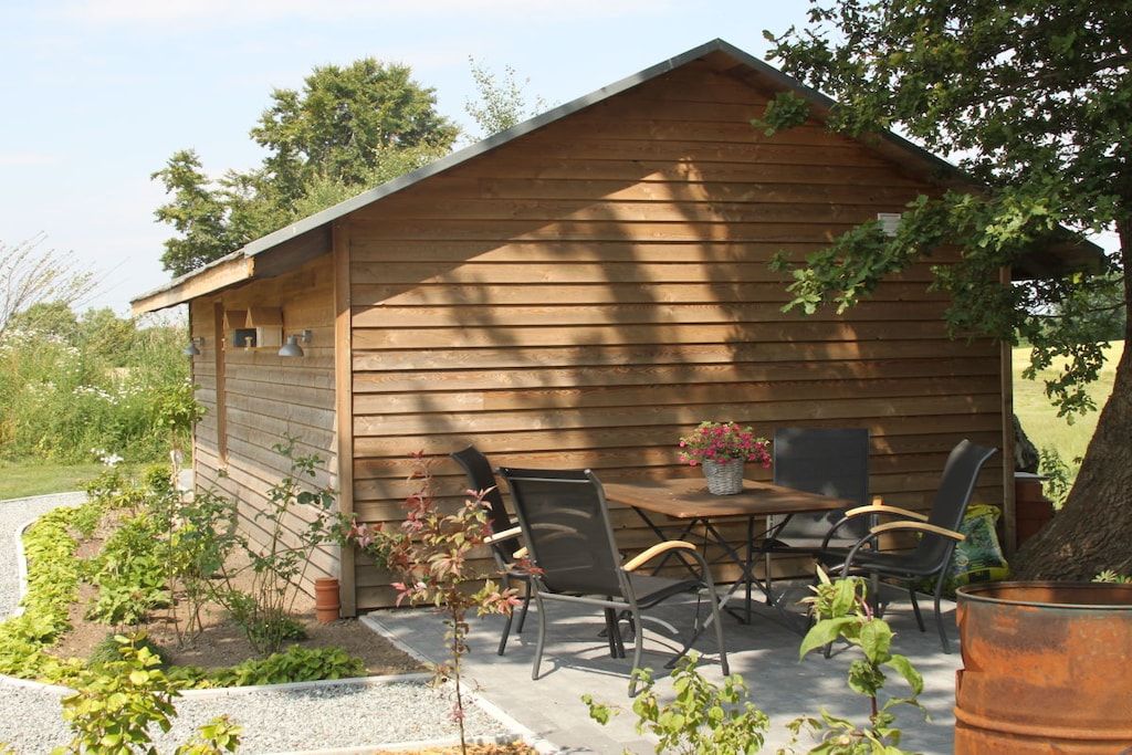 A wooden cabin with a dining table and chairs, surrounded by a garden.