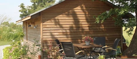A wooden cabin with a dining table and chairs, surrounded by a garden.