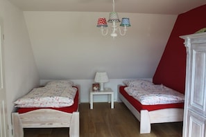 A bedroom with two single beds, a small white nightstand, a lamp, and a chandelier with patterned lampshades. - House Uhlenstraat - Apartment Käthe (Esgrus)
