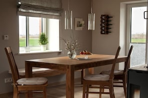 A dining area with a wooden table, four chairs, a vase with branches, and a window with a view of the outdoors. - House Uhlenstraat - Apartment Käthe (Esgrus)