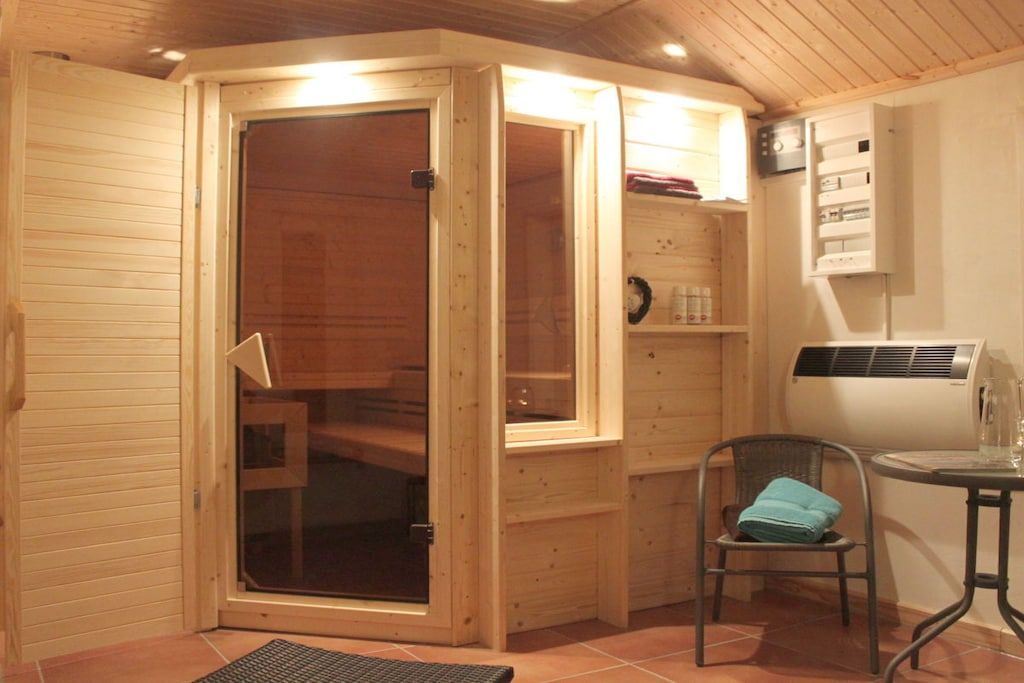 A wooden room with a sliding glass door, a chair, a small table, and a wall-mounted heater.