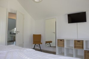 Ein Hotelzimmer mit einem Bett, einem Sessel, einem Fernseher, einem Spiegel und Korbwäsche.