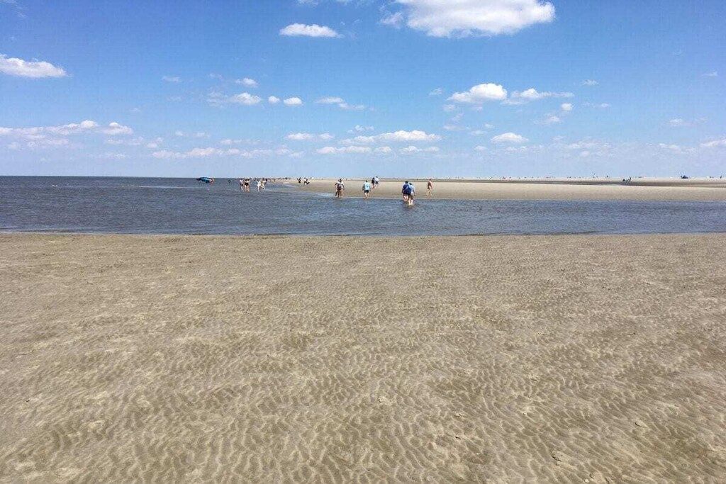 Een strand met helder water, een zandstrand en enkele mensen in de verte.