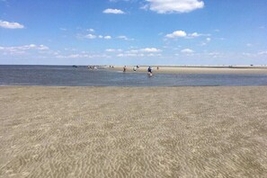 Een strand met helder water, een zandstrand en enkele mensen in de verte.