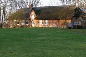 Een klassiek vakantiehuis met rieten dak, een auto op de oprit en een verzorgd gazon.