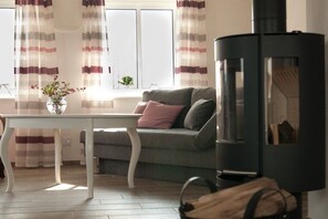 A living room with a sofa, a table, and a black wood-burning stove. - House Uhlenstraat - Apartment Theo (Esgrus)