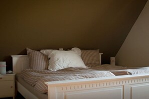 A bedroom with a sloped ceiling, a bed with striped bedding, and a nightstand with a lamp. - House Uhlenstraat - Apartment Theo (Esgrus)