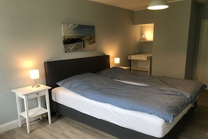 A bedroom with a bed, bedside tables, a nightstand, a wall-mounted shelf, and a painting. - Holiday apartment in Sörup with swimming pool (Sörup)