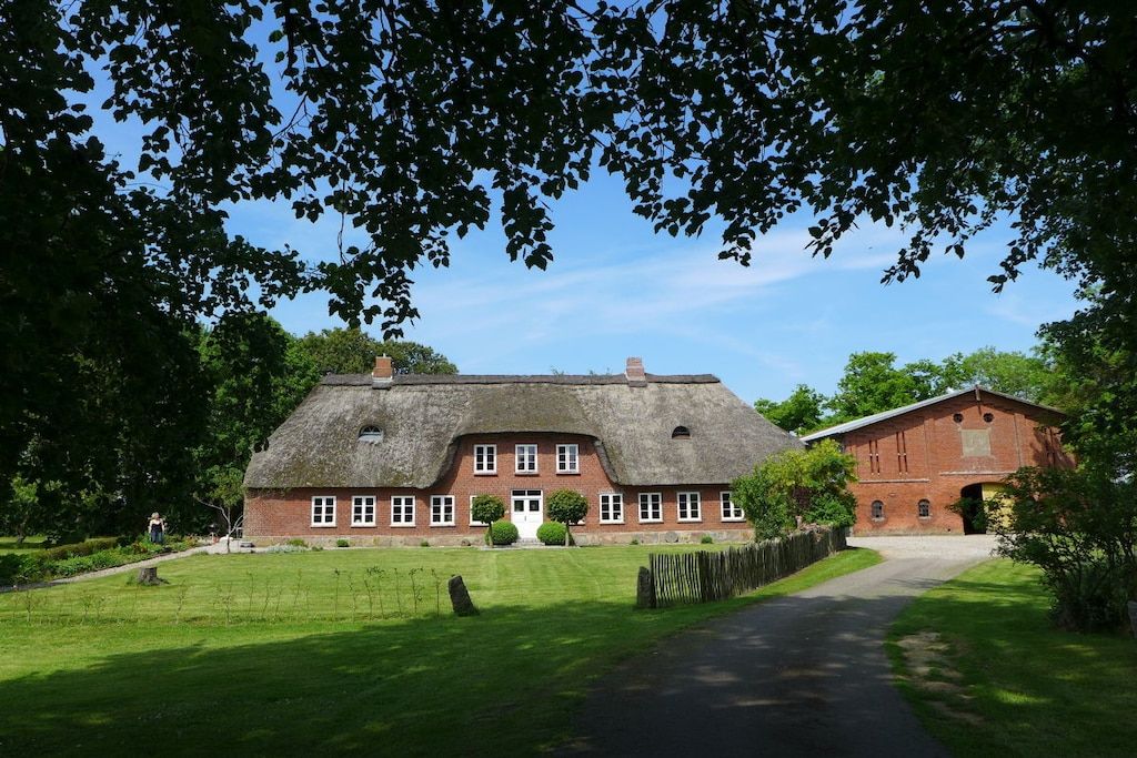 A traditional thatched-roof house with a brick extension, surrounded by a well-maintained lawn and a clear sky.
