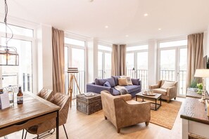 A modern living room with a sofa, armchairs, a coffee table, and a dining area with a table and chairs. - Holiday apartment with 1 bedroom (Lübeck Travemünde)