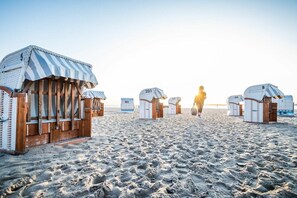 Beach huts with striped awnings and numbered doors, arranged on a sandy beach. - Holiday apartment with 1 bedroom (Lübeck Travemünde)