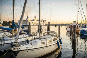 Een jachthaven met aangemeerde boten, een schip op de achtergrond en rustig water.