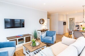 A modern living room with a flat-screen TV, a blue armchair, a wooden coffee table with a vase, and a sofa. - Holiday apartment with 1 bedroom (Lübeck Travemünde)