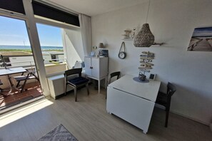 A compact kitchen with a dining area, a white refrigerator, a small cabinet, and a window overlooking a beach. - South Beach happiness (Burgtiefe-Südstrand)